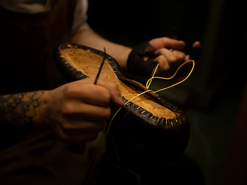 Artisan hand-stitching a custom-made leather shoe in the workshop